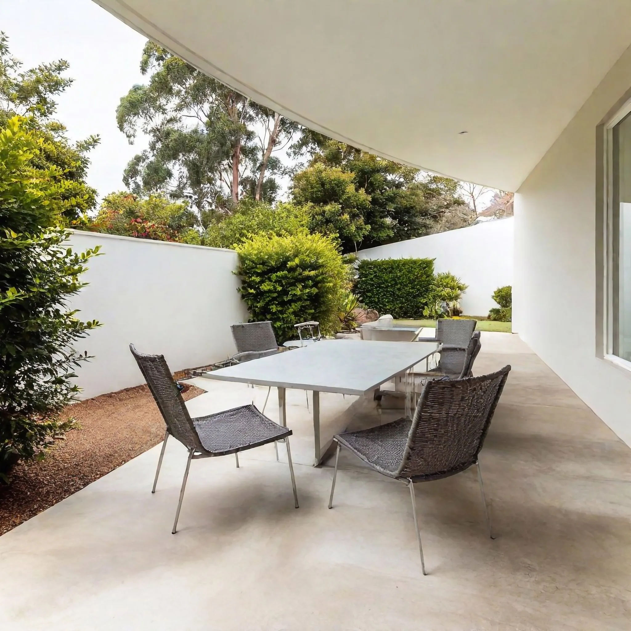 A covered concrete patio entertaining area beside a backyard pool